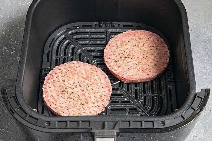 Frozen beef burger patties arranged in an air fryer basket