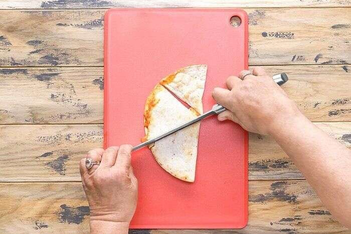 Air-fryer quesadilla being cut into wedges on a cutting board