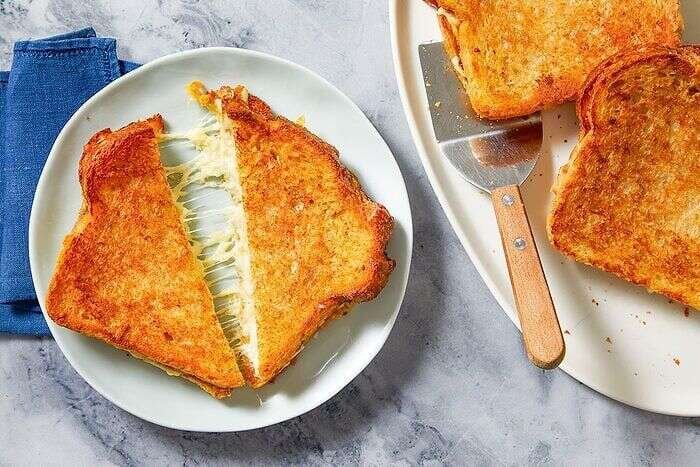 Golden grilled cheese sandwich cut in half with melted cheese pull