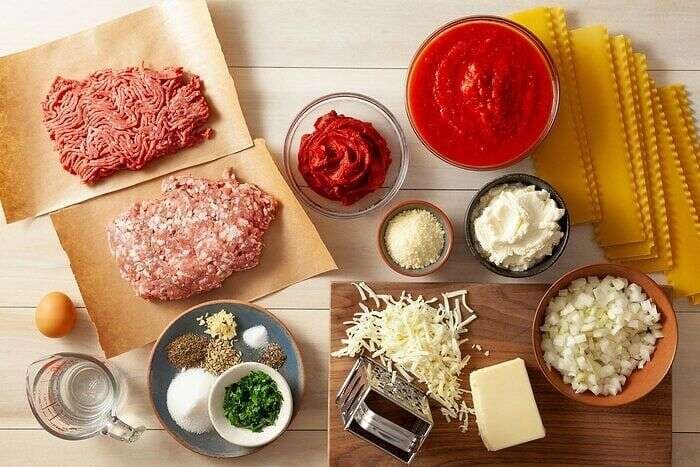 Ingredients for homemade lasagna with noodles, sausage, ground beef, tomatoes, and cheese