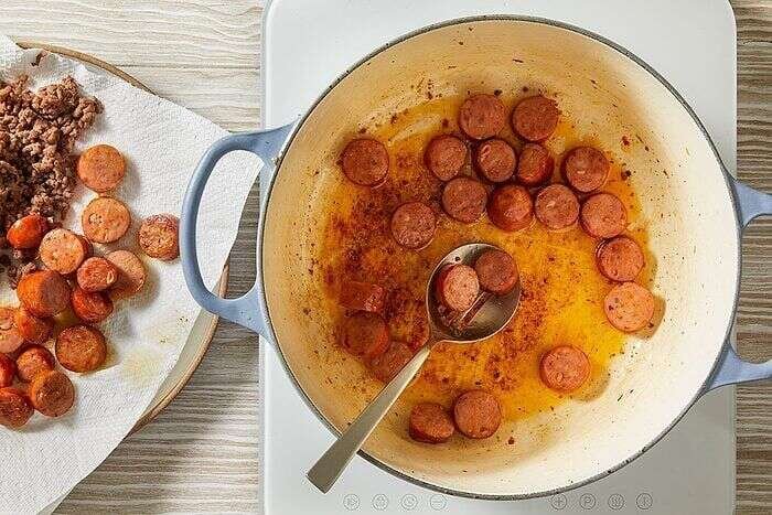 Sliced andouille sausage browning in a Dutch oven for dirty cabbage