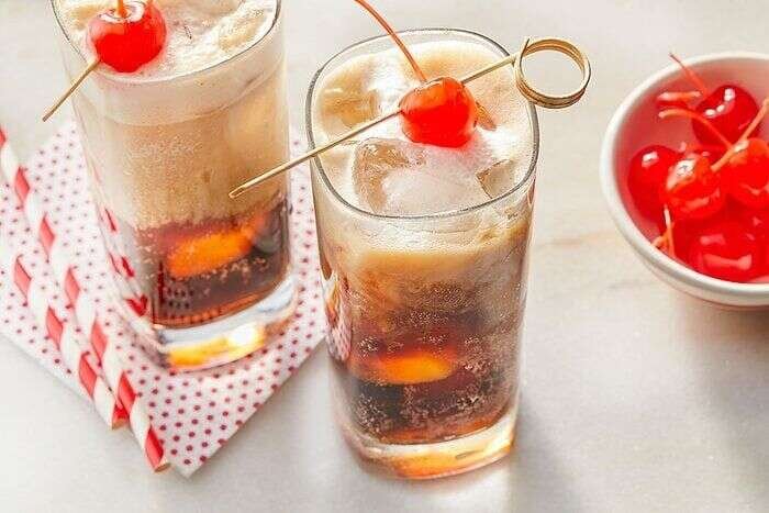 Two finished Dirty Dr Pepper drinks with creamy foam and maraschino cherries