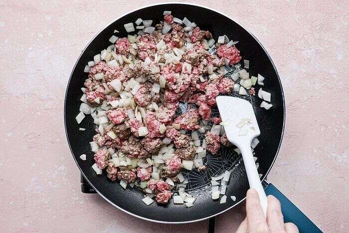 Ground beef and onion cooking in a skillet for Frito pie