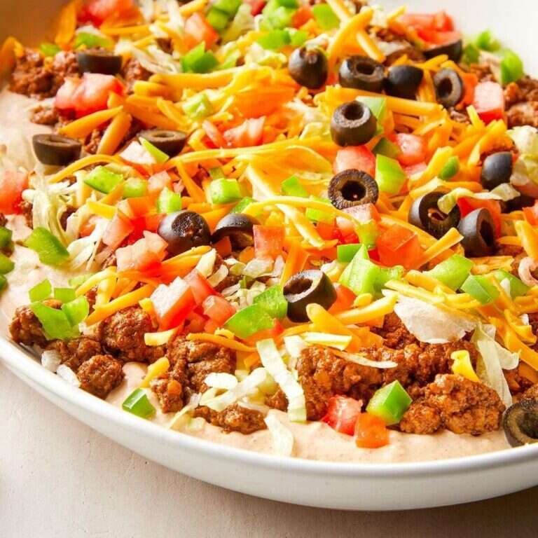 Easy Ground Beef Taco Dip Recipe for Parties Ground beef taco dip with creamy layers, cheddar, lettuce, tomatoes, peppers, and olives