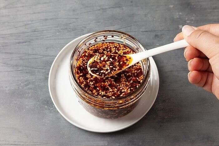Spoonful of homemade chili crisp showing crispy bits and red oil