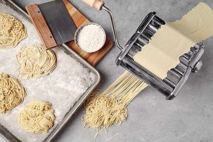 Fresh ramen noodles being cut with a pasta machine