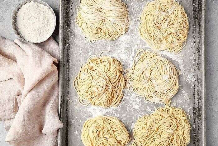 Fresh homemade ramen noodle nests on a floured baking sheet