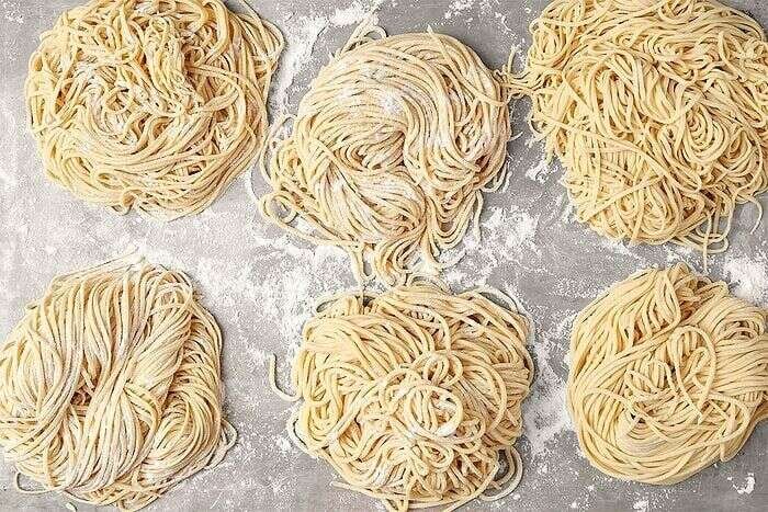 Fresh homemade ramen noodle nests arranged on a floured surface