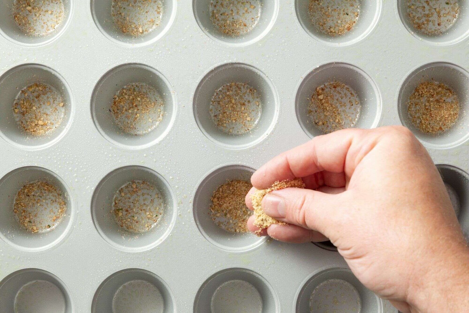 Breadcrumbs sprinkled into greased mini muffin cups for mac and cheese bites