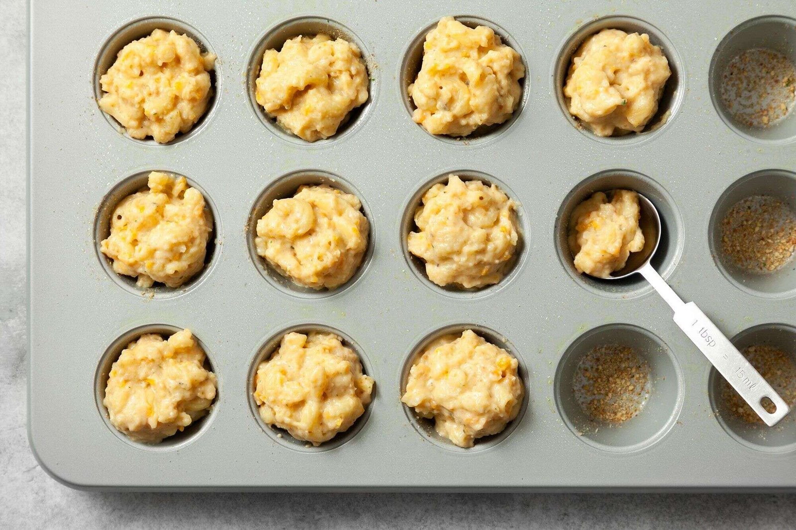 Mac and cheese mixture spooned into greased mini muffin cups