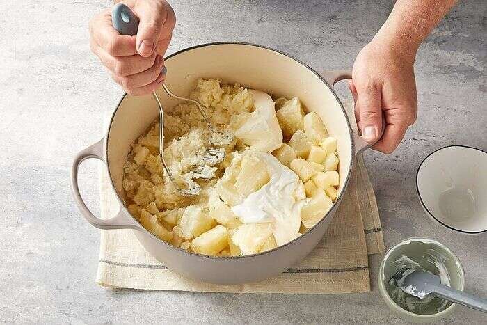 Mashing cooked potatoes with cream cheese sour cream and butter