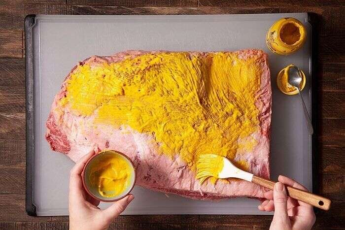 Brushing yellow mustard over both sides of a beef brisket