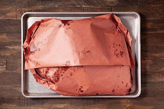Wrapped smoked brisket resting in a tray before slicing
