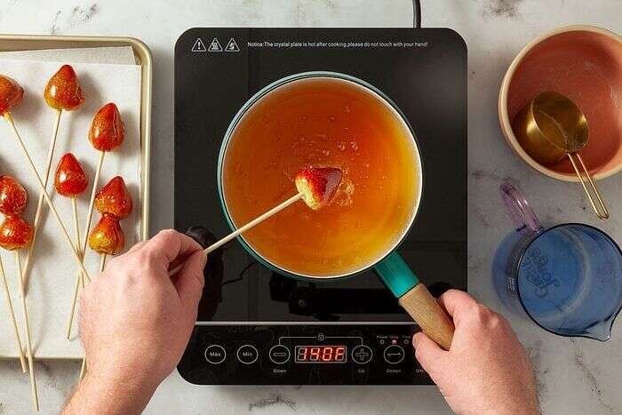 Strawberry being dipped into hot sugar syrup for tanghulu