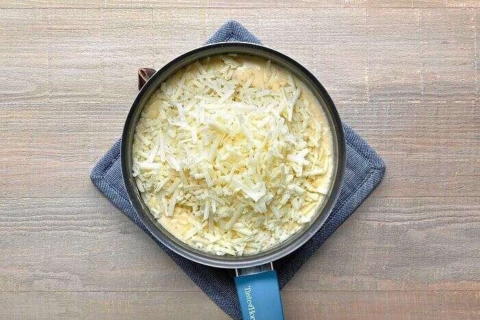 Sharp white cheddar and Manchego being added to the cheese sauce