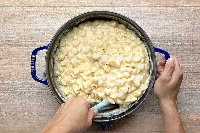 Creamy white cheddar cheese sauce being combined with cooked pasta